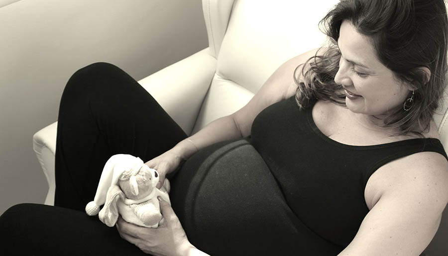 Pregnant mother sits on couch with a toy