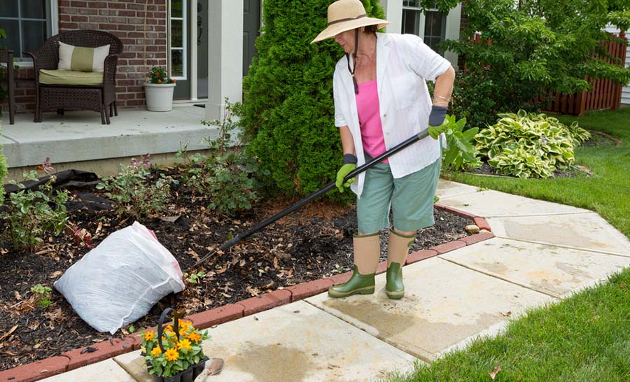 Une femme âgée ajoute du paillis au jardin et à l’aménagement paysager