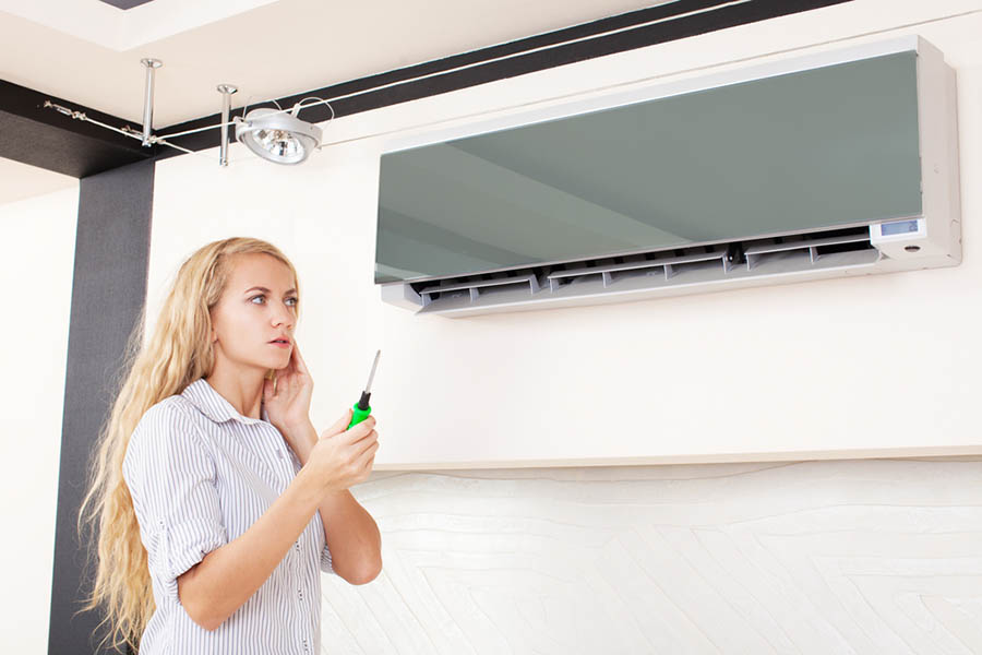 Women holds screwdriver with a confused look in front of wall air conditioner