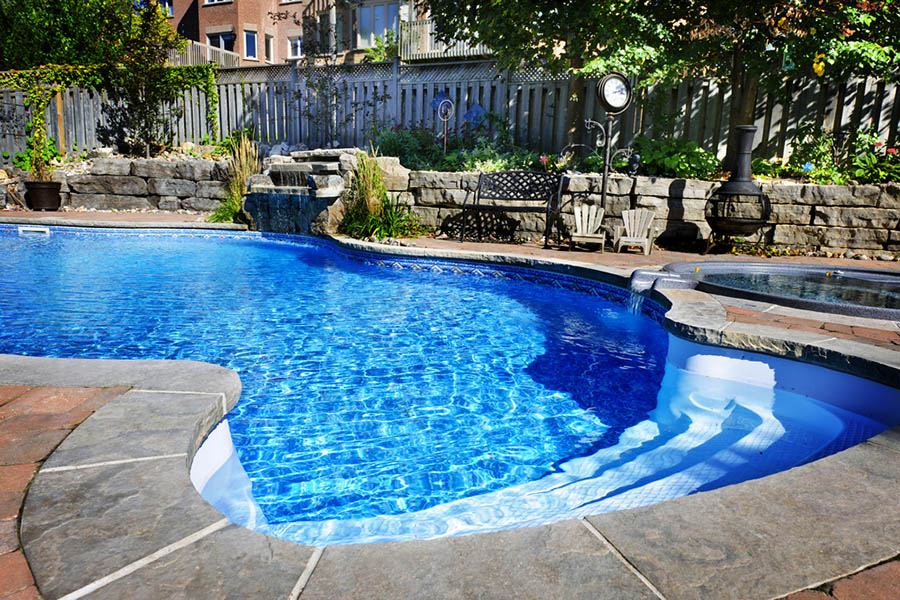 Backyard in ground pool with hot tub and surrounding landscaping