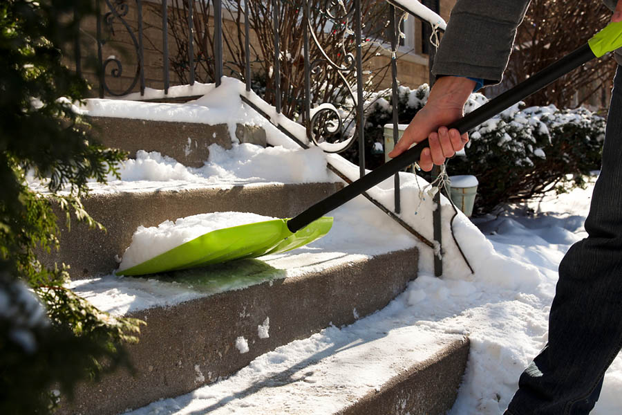 A person shovels snow from the stairs of their doorstep