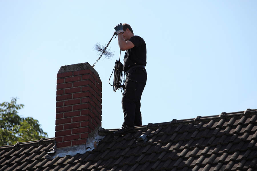 Un homme sur le toit nettoie une cheminée pour un poêle à bois