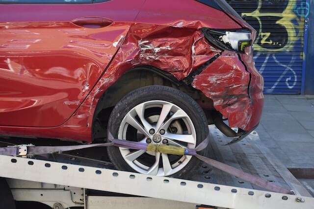 A red vehicle loaded onto a tow truck, with visible damage from a collision