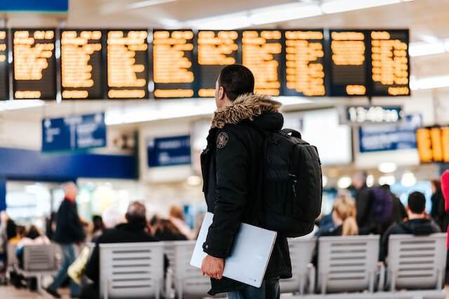 A person standing in an airport, staring at a departure/arrival board in the background