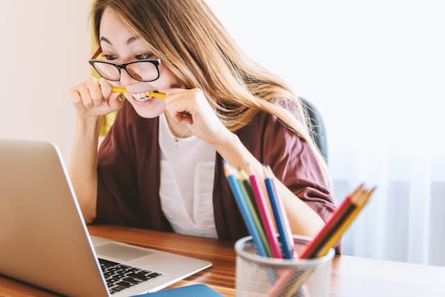 A person staring in confusion at their laptop while biting a pencil