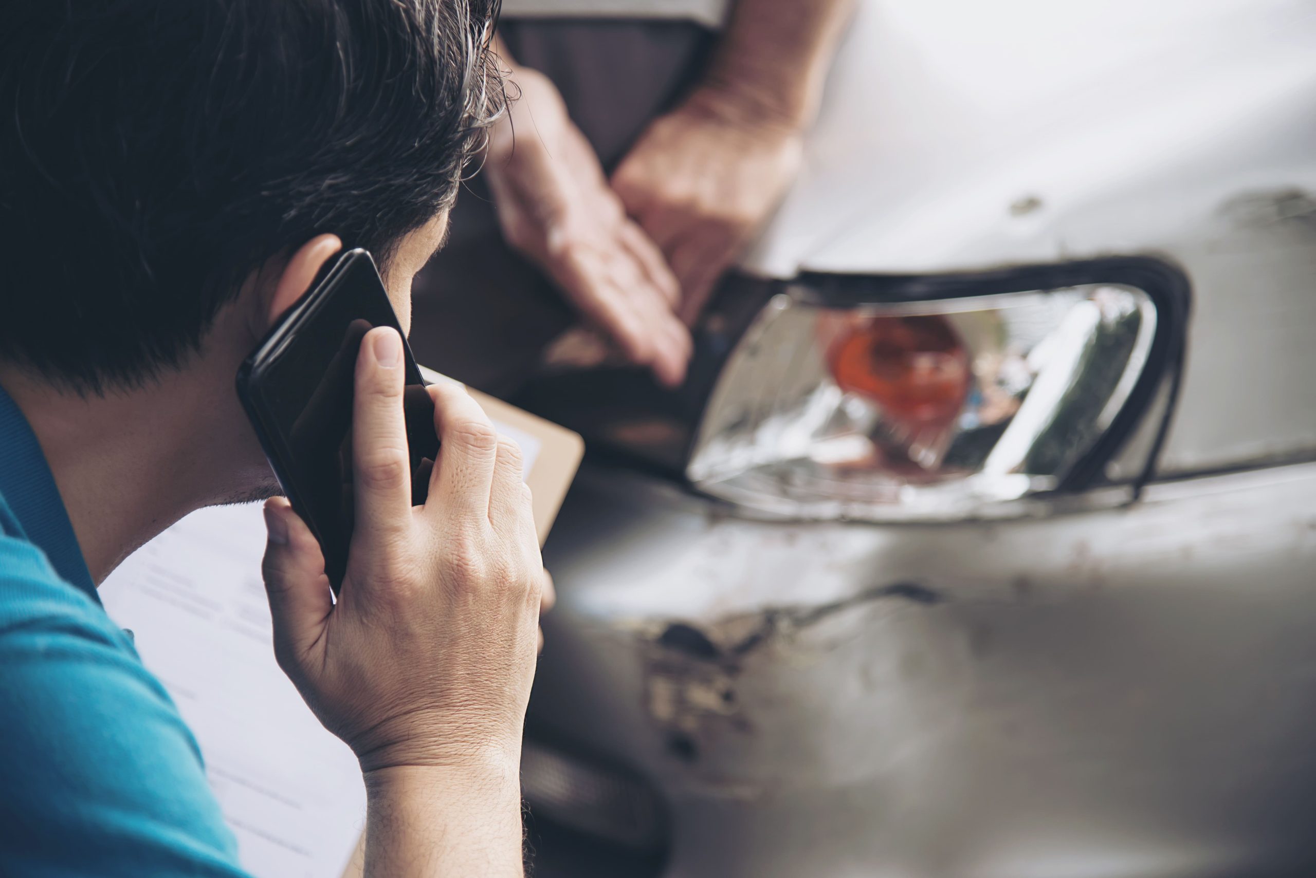 Insurance adjuster at a car accident site assessing the damage to a grey car's front fender bender