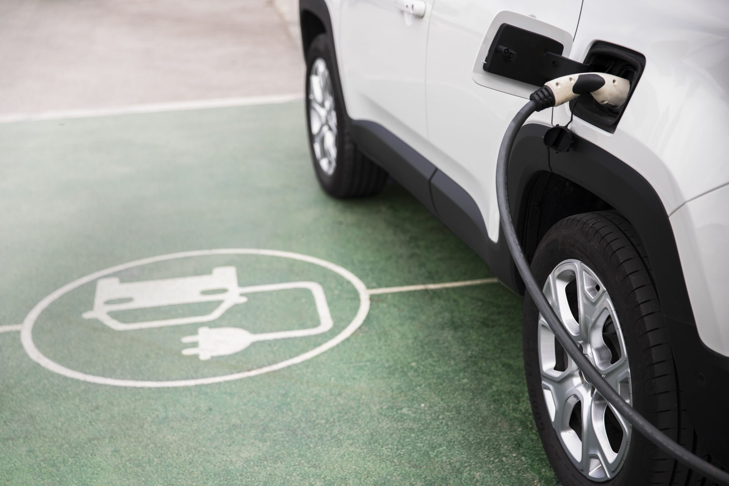 A white electric vehicle being charged at a charging station with green floor markings