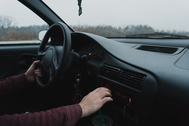 View from the passenger's seat of a car with a black interior on a rainy day, as the driver adjusts the radio