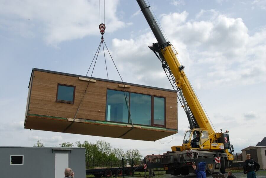A large crane lifts one module of a modular home into place